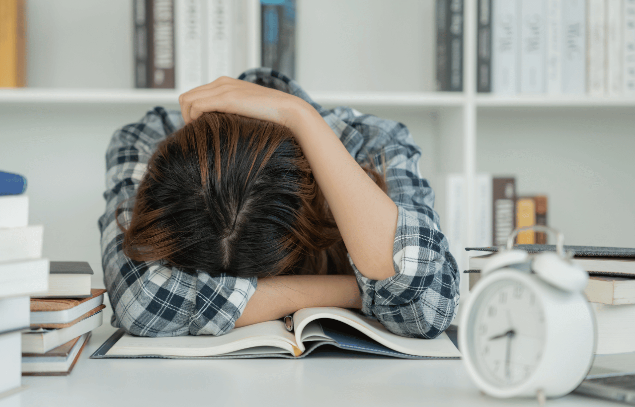 Stressed student studying with clock, books, and computer - Overcoming exam stress with hypnotherapy.